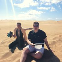Zwei junge Leute sitzen im Sand bei sonnigem Wetter