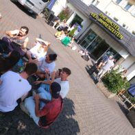 Eine Gruppe sitzt gemeinsam vor dem Rheinhotel Vier Jahreszeiten