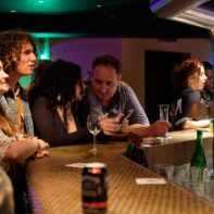 mehrere Mitarbeiter warten an der Bar auf ihre Getränke
