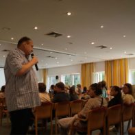 Ein Saal mit talk2move Mitarbeitern die in Stuhlreihen sitzen und dem Geschäftsführer zuhören