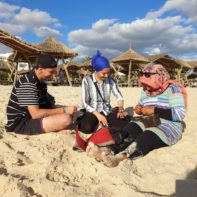 Zwei Fundraiser lassen sich von einer Einheimischen am Strand Henna-Tattoos machen