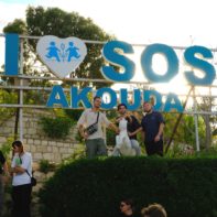 Drei Fundraiser posieren vor einem großen blauen "I-Love-SOS-Akouda"-Schild