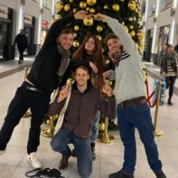 Vier Fundraiser die in einem Einkaufscenter vor einem Weihnachtsbaum posieren