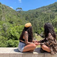 Zwei junge Frauen sitzen sich gegenüber auf der Ali Brücke und halten Händchen