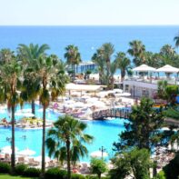 Ein Hotelresort direkt am Mittelmeer mit vielen großen Palmen und einem großen Pool mit Wasserrutsche.