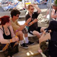 Eine Gruppe von fünf Personen sitzen am Strand un spielen Karten.